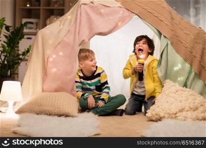 childhood, hygge and friendship concept - happy boys with torch light having fun in kids tent or teepee at home. happy boys with torch light in kids tent at home. happy boys with torch light in kids tent at home