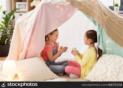 childhood, hygge and friendship concept - little girls playing clapping game in kids tent or teepee at home. girls playing clapping game in kids tent at home. girls playing clapping game in kids tent at home