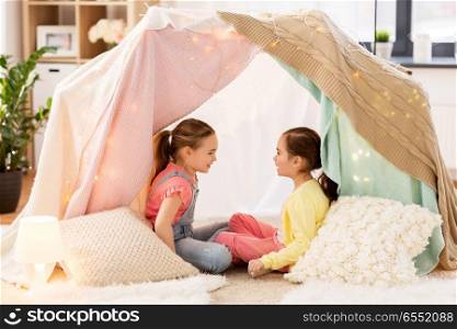 childhood, hygge and friendship concept - little girls talking in kids tent or teepee at home. little girls talking in kids tent at home. little girls talking in kids tent at home