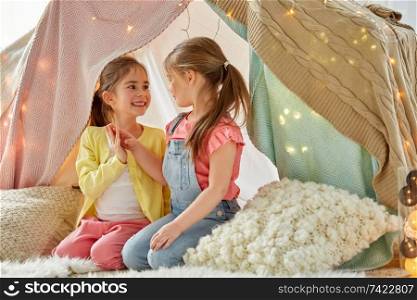 childhood, hygge and friendship concept - little girls talking in kids tent or teepee at home. little girls talking in kids tent at home