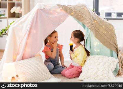 childhood, hygge and friendship concept - little girls with torch light having fun in kids tent or teepee at home. little girls with torch light in kids tent at home. little girls with torch light in kids tent at home