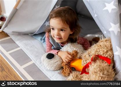 childhood, hygge and people concept - happy little baby girl playing with toys in kid’s tent or teepee at home. baby girl playing with toys in or teepee at home