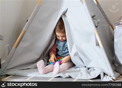 childhood, hygge and people concept - little baby girl playing with simple dimple toy in kid&rsquo;s tent or teepee at home. girl playing with fidget toy in teepee at home