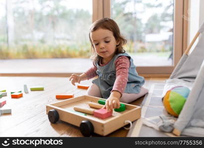 childhood, hygge and people concept - little baby girl playing with toy blocks at home. happy baby girl playing with toy blocks at home