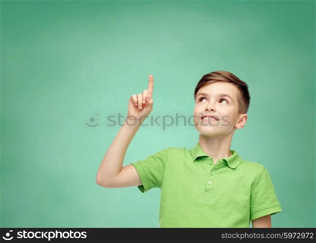 childhood, idea, education and people concept - happy smiling boy in green polo t-shirt pointing finger up over green school chalk board background