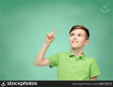 childhood, idea, education and people concept - happy smiling boy in green polo t-shirt pointing finger up over green school chalk board background