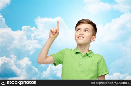 childhood, idea, inspiration and people concept - happy smiling boy in green polo t-shirt pointing finger up over blue sky and clouds background