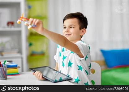childhood, imagination and technology concept - happy little with tablet pc computer and toy airplane at home. boy with tablet computer and toy airplane at home