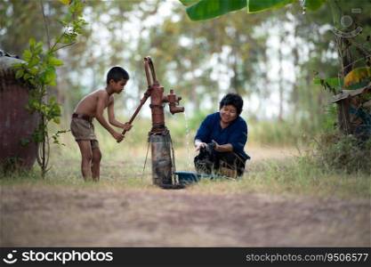 Childhood in rural Thailand. A small child assists his family by pumping natural water into a bucket to be used in everyday life