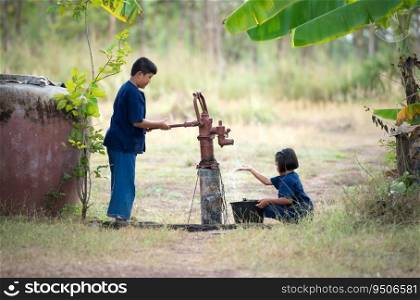 Childhood in rural Thailand. A small child assists his family by pumping natural water into a bucket to be used in everyday life