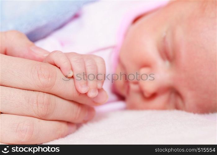 Childhood innocence concept. Little adorable newborn baby sleeping on bed holding mother hand. Baby sleeping in blanket holding mother hand