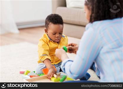 childhood, kids and people concept - african american mother and her baby son playing together with wooden toy blocks kit on floor at home. mother and baby playing with toy blocks at home