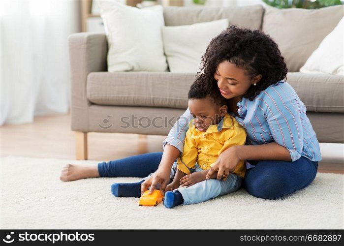 childhood, kids and people concept - happy african american mother and her baby son playing with toy car together on sofa at home. mother and baby playing with toy car at home