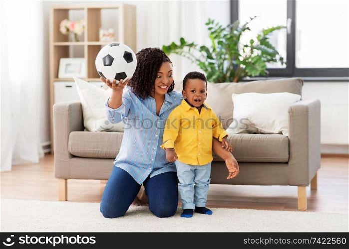 childhood, kids and people concept - happy african american mother and her baby son playing with soccer ball together on sofa at home. mother and baby playing with soccer ball at home
