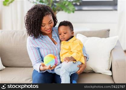 childhood, kids and people concept - happy african american mother and her baby son playing with ball together on sofa at home. mother and baby playing with ball at home
