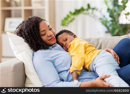 childhood, kids and people concept - happy african american mother with her baby son lying on sofa at home. happy african american mother with baby at home