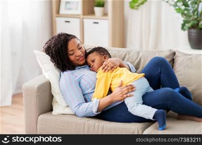childhood, kids and people concept - happy african american mother with her baby son lying on sofa at home. happy african american mother with baby at home