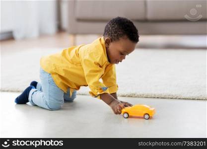 childhood, kids and people concept - lovely african american baby boy playing with yellow toy car on floor at home. african american baby boy playing with toy car