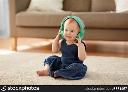 childhood, kids and technology concept - lovely redhead baby girl in headphones listening to music at home. redhead baby girl in headphones listening to music. redhead baby girl in headphones listening to music