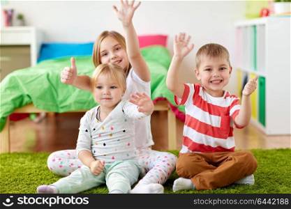 childhood, leisure and family concept - group of happy kids sitting on floor at home and waving hands. group of happy kids sitting on floor at home