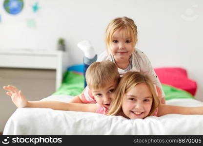 childhood, leisure and family concept - happy little kids having fun in bed at home. happy little kids having fun in bed at home. happy little kids having fun in bed at home