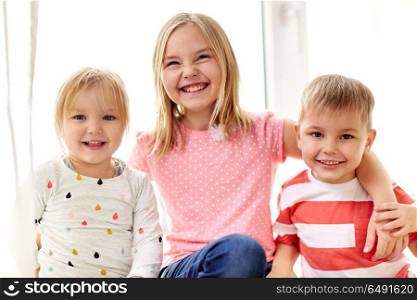 childhood, leisure and family concept - happy little kids hugging at window. happy little kids hugging at window. happy little kids hugging at window