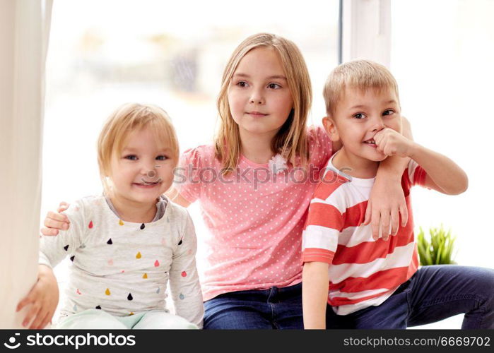 childhood, leisure and family concept - happy little kids hugging at window. happy little kids hugging at window. happy little kids hugging at window