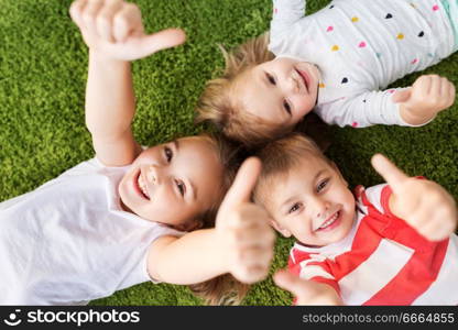 childhood, leisure and family concept - happy little kids lying on floor or carpet and showing thumbs up. happy kids lying on floor and showing thumbs up