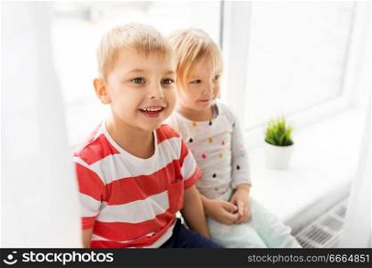 childhood, leisure and family concept - happy little kids sitting on window sill. happy little kids sitting on window sill