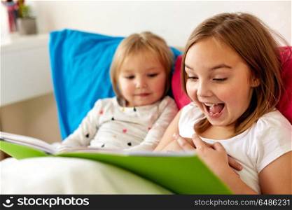 childhood, leisure and family concept - little girls or sisters reading book in bed. little girls or sisters reading book in bed. little girls or sisters reading book in bed