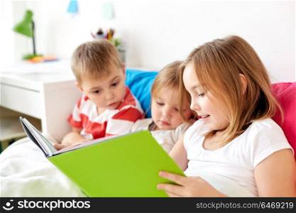 childhood, leisure and family concept - little kids reading book in bed at home. little kids reading book in bed at home