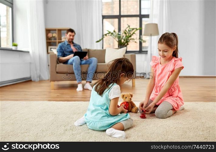 childhood, leisure and family concept - little sisters playing tea party game with toy crockery and teddy bear at home. girls playing with toy crockery and teddy at home