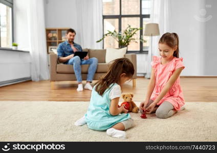 childhood, leisure and family concept - little sisters playing tea party game with toy crockery and teddy bear at home. girls playing with toy crockery and teddy at home