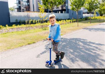 childhood, leisure and fun concept - happy little boy riding scooter in city. happy little boy riding scooter in city