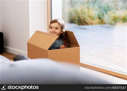 childhood, leisure and moving concept - little baby girl sitting inside cardboard box at home. little baby girl sitting in cardboard box at home
