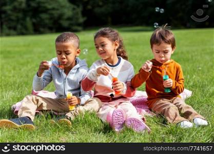 childhood, leisure and people concept - group of children blowing soap bubbles at park. group of children blowing soap bubbles at park