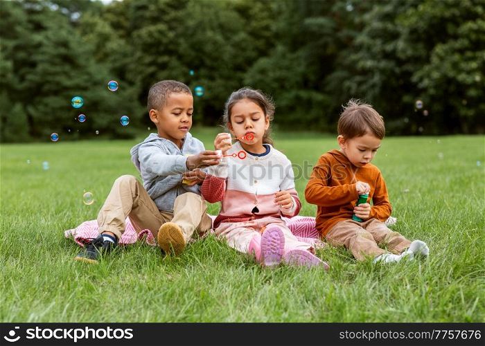 childhood, leisure and people concept - group of children blowing soap bubbles at park. group of children blowing soap bubbles at park