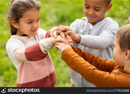 childhood, leisure and people concept - group of children stacking hands at park. group of children stacking hands at park
