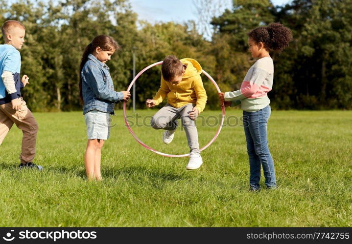 childhood, leisure and people concept - group of happy children jumping through hula hoop at park. happy children jumping through hula hoop at park
