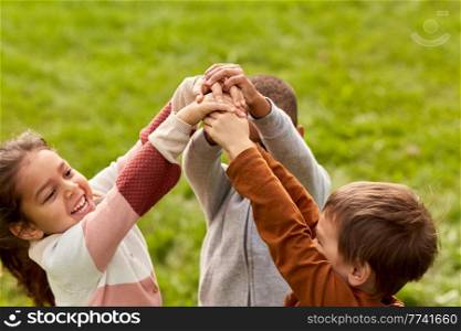 childhood, leisure and people concept - group of happy children playing and stacking hands at park. happy children playing and stacking hands at park