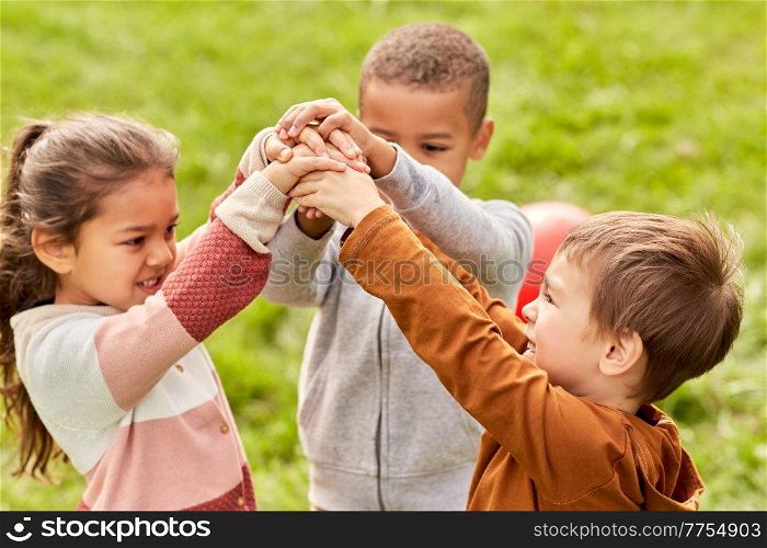 childhood, leisure and people concept - group of happy children playing and stacking hands at park. happy children playing and stacking hands at park