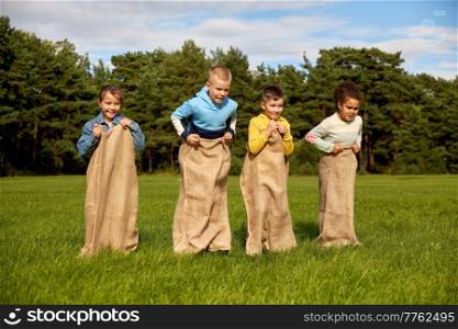 childhood, leisure and people concept - group of happy children playing bag jumping game at park. happy children playing bag jumping game at park