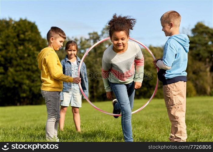 childhood, leisure and people concept - group of happy children playing game with hula hoop at park. happy children playing game with hula hoop at park