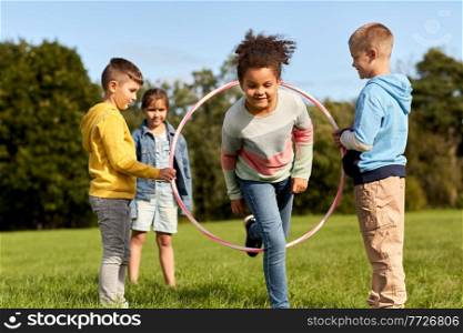 childhood, leisure and people concept - group of happy children playing game with hula hoop at park. happy children playing game with hula hoop at park