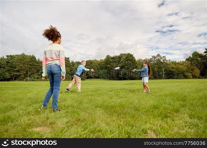 childhood, leisure and people concept - group of happy children playing game with flying disc at park. happy children playing with flying disc at park