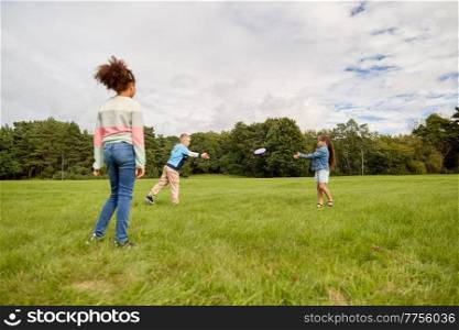childhood, leisure and people concept - group of happy children playing game with flying disc at park. happy children playing with flying disc at park