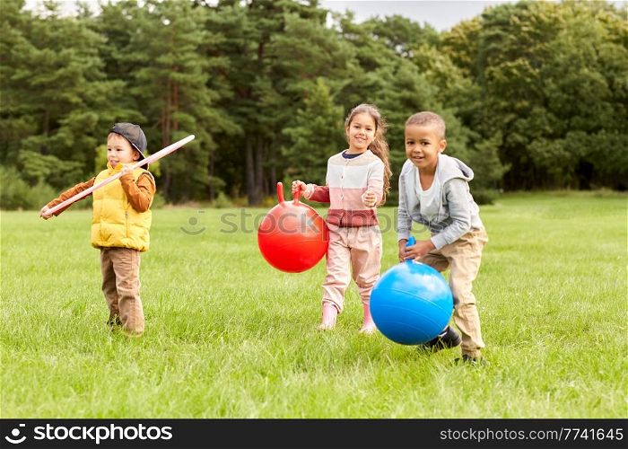 childhood, leisure and people concept - group of happy children playing with hopper balls and hula hoop at park. children playing with hoppers and hoop at park