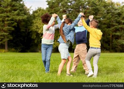 childhood, leisure and people concept - group of happy kids playing round dance at park. happy children playing round dance at park