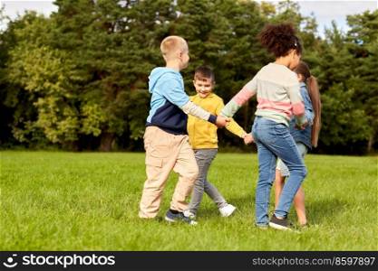childhood, leisure and people concept - group of happy kids playing round dance at park. happy children playing round dance at park