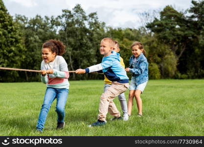 childhood, leisure and people concept - group of happy kids playing tug-of-war game and running at park. happy children playing tug-of-war game at park